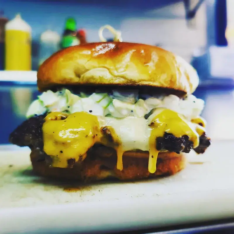 Delicious burger from Lib's Diner with melted cheese, creamy coleslaw, and a golden brioche bun, perfect for a brewery event.